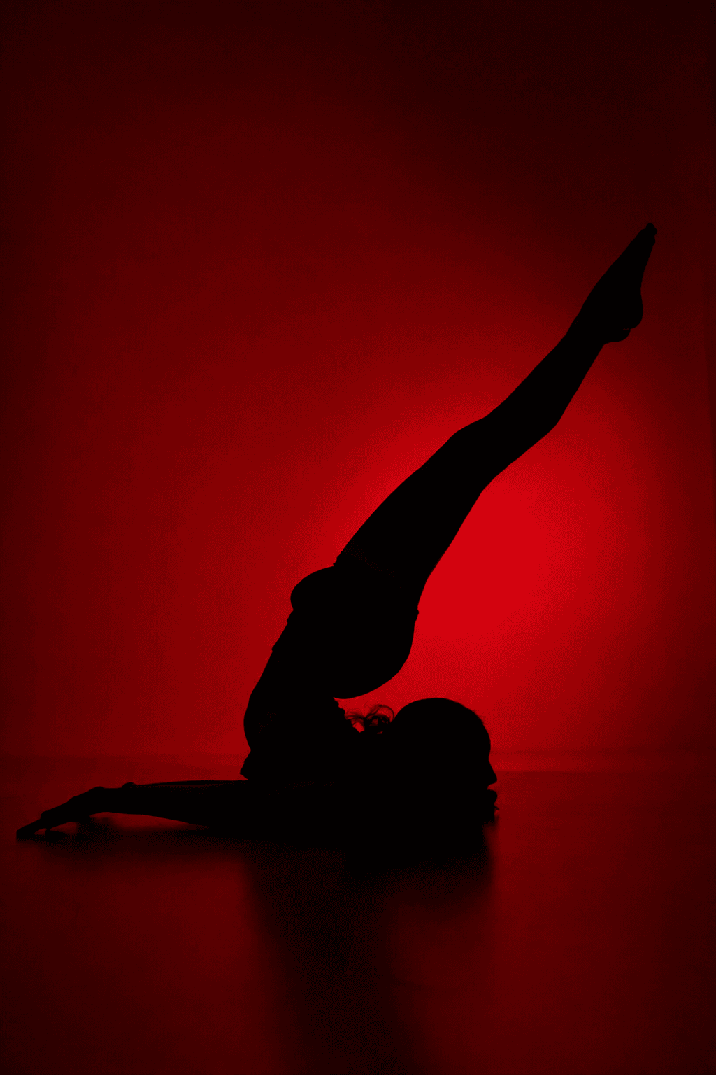 Silhouette in a deep backbend, leg extended, lit in infrared red